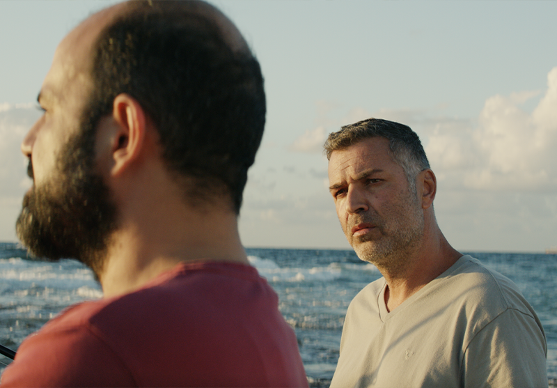 Two men converse on a beach.