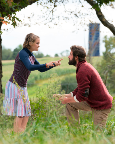 a young girl uses sign language to communicate with her father. Still from the quiet place. They are in a field, he kneels and she stands over him