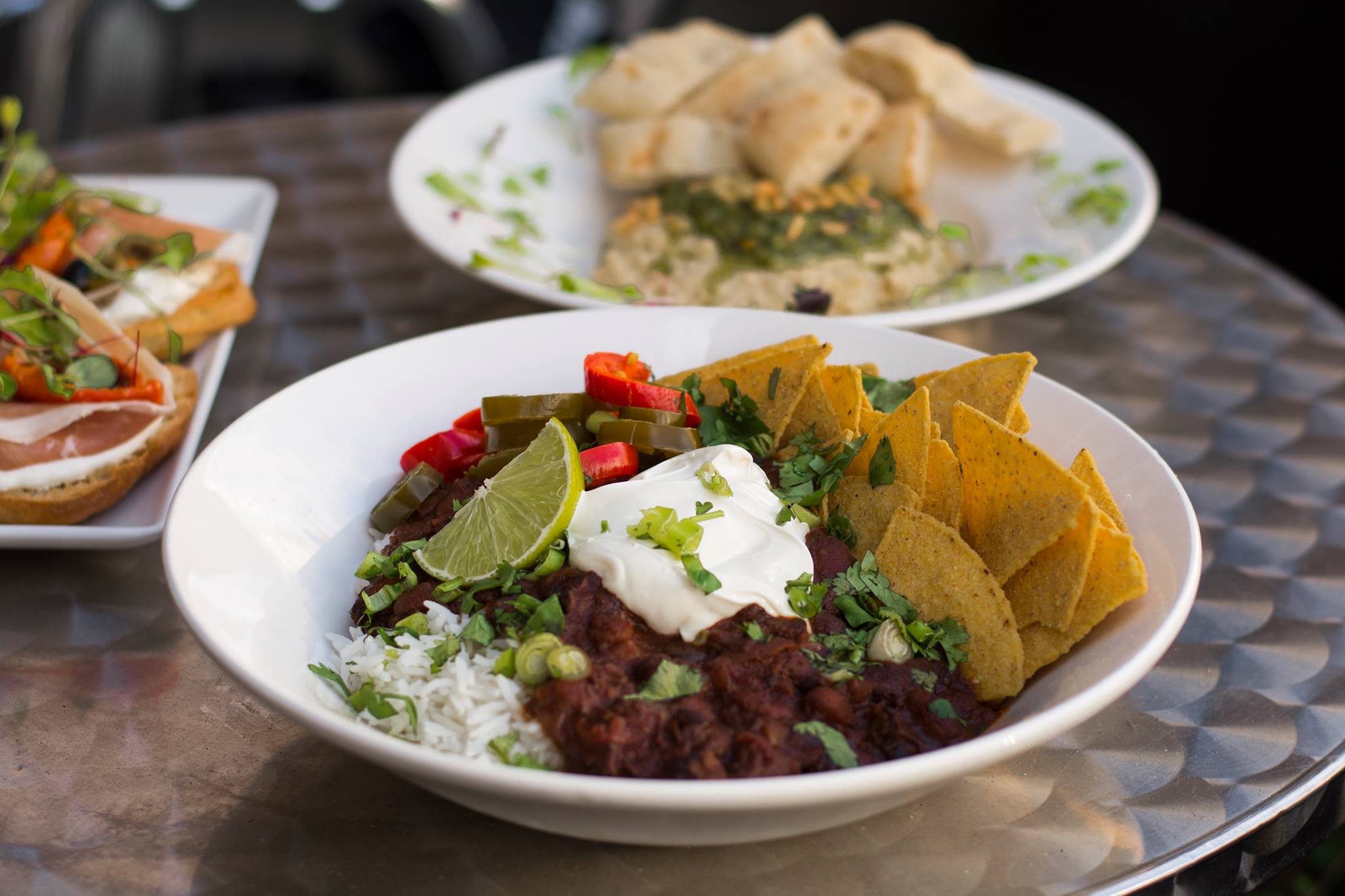 Filmhouse Nachos sit in a large bowl on a silver outside table along with two other dishes blurred in the background